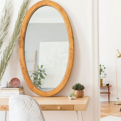 Oval wooden mirror above desk with decor items, living room view reflected