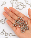 Hand holding Heavy Duty 1 Inch Eye Screws Hooks Set 150 Pack Screw Eyes For Wood Hanging Artwork Ropes And Light Loads Tough As Nails Pro Grade Iron Ring Bolts For Indoor Outdoor Use