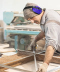 Man wearing Six Pack Adjustable Safety Ear Muffs For Noise Reduction And Hearing Protection All Day Comfort For Hunting Shooting Construction And Woodworking Blue while working in a woodworking shop.