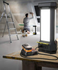 Tower Work Light Delivers 9000 Lumen Brightness With Full 360 Degree Illumination, Three Dimmable Panels, Two 120V Outlets And USB A Port For Tools, Projects, And On The Job Site Lighting, illuminating a workshop with a man sanding in the background.