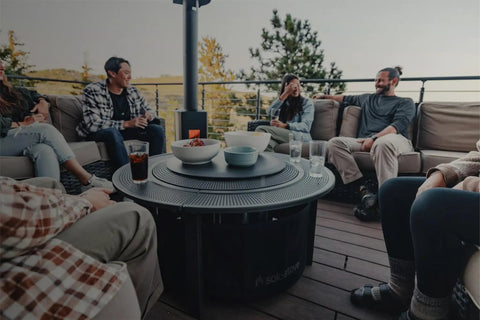 People gathered around a Surround Surface Fire Pit Lid For Bonfire And Ranger Pits Built For The Backyard Boss Vibe Durable Cold Rolled Steel Cover 23.75 Inch Diameter 7.05 Lb Weight Converts To A Sleek Outdoor Tabletop on a deck.