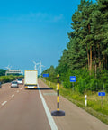 Heavy Duty Elastic Warning Bollard Post With Rock Solid Bounce Back Shield in traffic lane beside vehicles on highway.