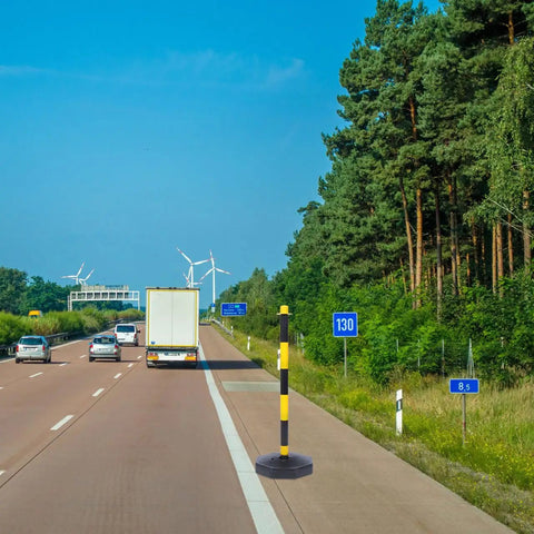 Heavy Duty Elastic Warning Bollard Post With Rock Solid Bounce Back Shield in traffic lane beside vehicles on highway.