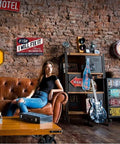 Vintage Metal Man Cave Sign For Men If I Say I Will Fix It There Is No Need To Remind Me Every 6 Months Funny Garage Wall Decor For Workshop Basement And Home Bar 12 X 8 Inches displayed in a stylish room with brick walls, next to a leather couch and guitar.