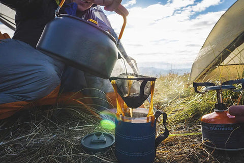Ultralight Java Drip Pour Over Coffee Maker For Camping And Backpacking Collapsible on grass next to camp stove