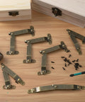 Six Piece Antique Brass Lid Support Folding Hinges For Jewelry Boxes And Wooden Cabinets with screws on a wooden table