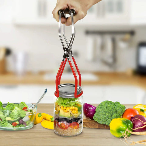 Hand holding jar lifter with red handles, lifting jar filled with vegetables in kitchen