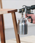 Stationary Hvlp Finishing Sprayer For Woodworkers Wanting Killer Results On Furniture Restoration Projects Using Pro Grade Metal Spray Gun aimed at a wooden stool.