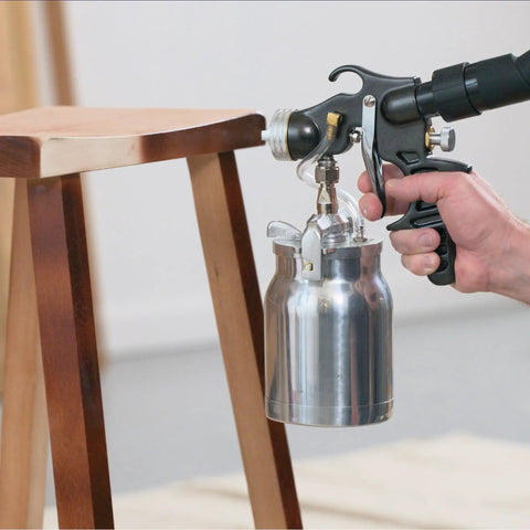 Stationary Hvlp Finishing Sprayer For Woodworkers Wanting Killer Results On Furniture Restoration Projects Using Pro Grade Metal Spray Gun aimed at a wooden stool.