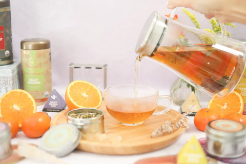Top Tier Double Walled Insulated Teapot That Keeps Your Daily Brew Sizzling Hot With Slick Stainless Steel Filter Lid For Loose Leaf Tea pouring tea into a glass cup surrounded by citrus fruits.