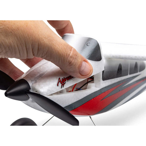 Close-up of hand lifting RC Airplane Apprentice STOL S 700 RTF With AS3X SAFE Technology, showcasing red and white fuselage design