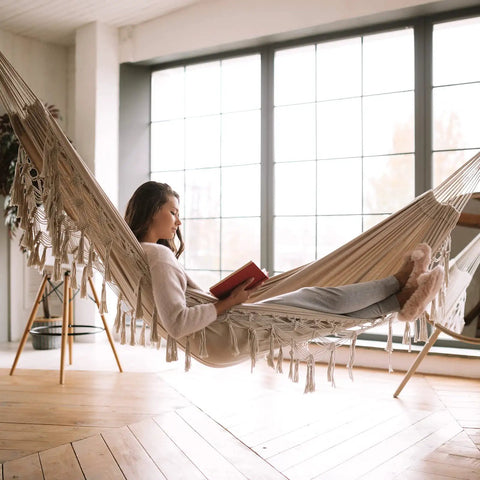 Person lounging in a heavy duty double hammock with 500 lb load capacity, tassel trim, fishtail knit design, indoors