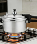 Stainless steel pressure cooker with black handles on a gas stove.