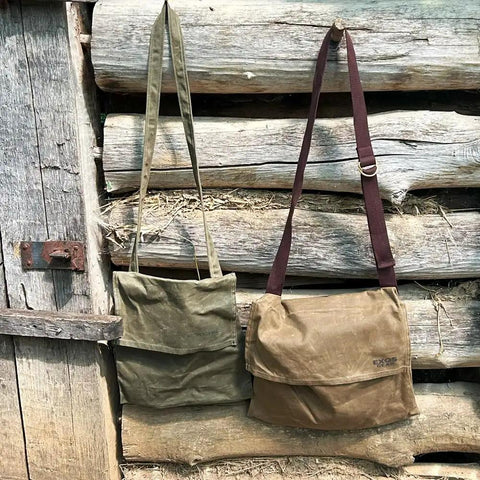 Two waxed canvas haversack outdoor bushcraft shoulder bags hanging on a wooden wall, showing water resistant design and dark khaki color.
