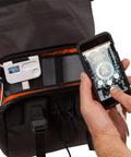 Inside view of Alpha Handlebar Bag 6 Liter for City Commutes and Bike Tours, Weatherproof Messenger With Roll Top And Tech Pocket, Recycled Materials, Black, Integrates With Joey T3 Smartbag Console For Power, Timer, LED Light, And Clock, shown with tech connected to smartphone.