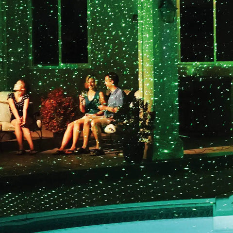 Outdoor scene with Motion Laser Holiday Projector With Thousands Of Lights, illuminating friends on patio with moving light modes.