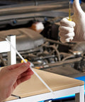 Hand holding a white plastic welding rod in a garage, demonstrating Grab These 10 Pc Plastic Welding Rods For Car Bumper Repair.