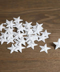White Mini Metal Barn Stars Set of 27 for Crafts Handcrafted 1 Inch Metal Ornaments with Antique Finish displayed on wood surface