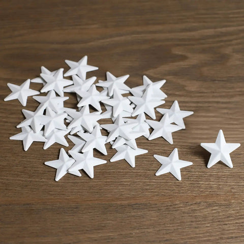 White Mini Metal Barn Stars Set of 27 for Crafts Handcrafted 1 Inch Metal Ornaments with Antique Finish displayed on wood surface