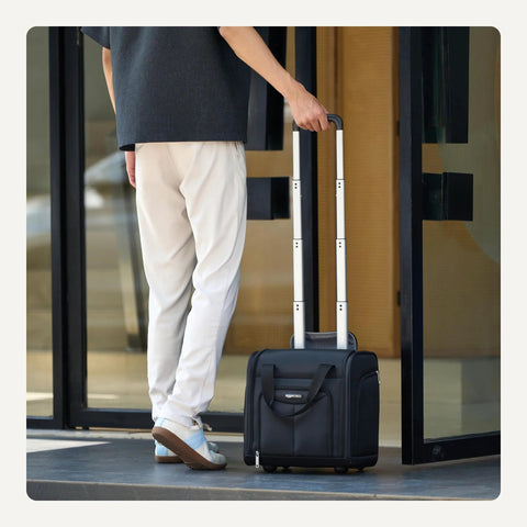 Side view of a person pulling a black Amazon Basics 14-inch underseat rolling luggage with extended handle