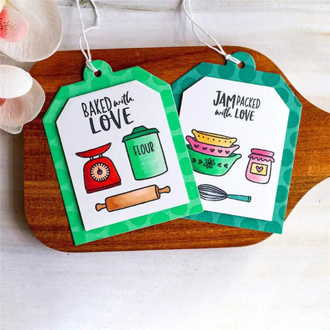 Two decorative kitchen-themed tags with baking illustrations and phrases 'Baked with Love' and 'Jam Packed with Love' on a wooden board.