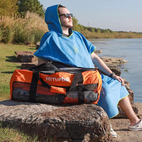 Man sitting by lake with 100L Mesh Dive Duffel Bag For Scuba Gear And Water Sports - Beast Large Gear Bag in orange and black on a rock.