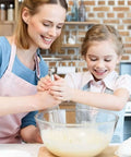 A mother and daughter using an 8-inch Go-To Stainless Steel Balloon Whisk Set in a kitchen to blend batter in a clear mixing bowl.
