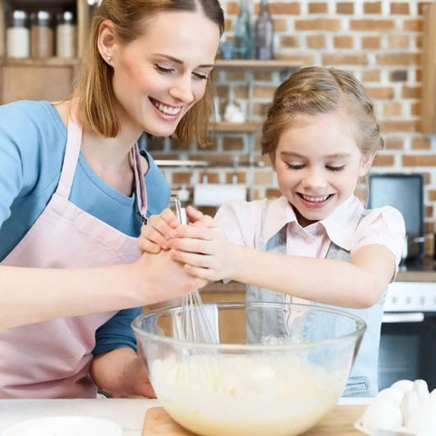 A mother and daughter using an 8-inch Go-To Stainless Steel Balloon Whisk Set in a kitchen to blend batter in a clear mixing bowl.
