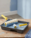 Knockout Paint Roller One Pack With A Legit Synthetic Fiber Cover And Dual Yellow Stripes To Slam Missed Spots And Serve Up Butter Smooth Coverage For Any Weekend Warrior DIY Project in a paint tray with blue paint.