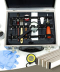 Front view: aluminum tool case with black interior containing assorted hand tools, brushes, magnifying glass, and tape measure.