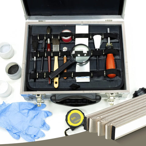 Front view: aluminum tool case with black interior containing assorted hand tools, brushes, magnifying glass, and tape measure.