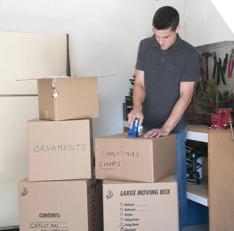 Person using Six Roll Pack Of High Performance Clear Packing Tape Refills For Shipping Moving Mailing And Storage Boxes, 1.88 Inch Wide By 60 Yard Length, 3 Inch Core, All Weather Grip And Super Strong Adhesive to seal boxes in a garage setting.