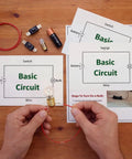 Hands assembling Electric Circuit Kit For Beginners 24 Piece Component Set with Light Bulb Wires Battery Holder Instructions on Table