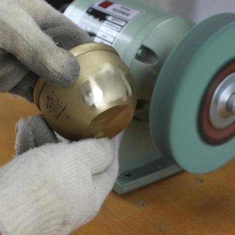 Hand holding brass object near bench grinder using Premium Elastic Polyurethane Buffing Wheels 6 Inch 2000 Grit Silicon Carbide Abrasive.