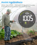 Farmer in greenhouse using CO2 monitor to optimize photosynthesis for plant growth, display shows 1005 ppm CO2