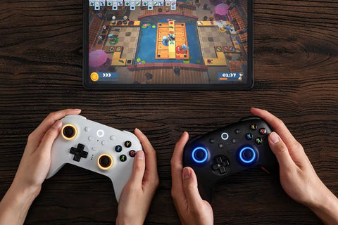 Hands holding white and black Wireless Gaming Controller For Windows PC Mac Steam And Android with RGB Fire Ring on wooden table.