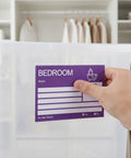 Hand placing Color Coded Moving Box Labels 160 Pack With Writable Notes Area 6x4 Inches on a storage bin.