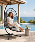 Woman relaxing on Comfy Hanging Egg Chair With Leg Rest And Stand In Gray by poolside, featuring rattan wicker and UV resistant cushion.