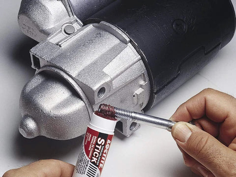 Loctite 37701 red high-strength threadlocker stick, 9 g, applied to metal threads near a motor housing.