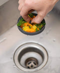 Hand holding Kitchen Sink Strainer 3.25 Inch Anti Clog Food Catcher Flexible Drain Basket Dishwasher Safe Standard Fit Made In USA Gray 2 Pack Rimless Design For Easy Water Flow And Mess Free Cleanup above drain