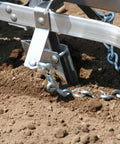 Close-up of the Pro Grade Precision Garden Seeder with 7 seed plates, aluminum body, working in soil, sweet corn planter visible.
