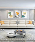 Modern living room with a long white sofa, abstract wall art, and a round coffee table viewed from the front.