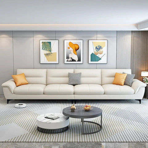 Modern living room with a long white sofa, abstract wall art, and a round coffee table viewed from the front.