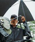 Person holding Universal Umbrella Holder Clamp For Round Or Oval Tubing on golf cart, steadying umbrella in wind.