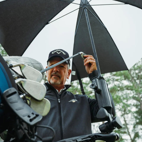 Person holding Universal Umbrella Holder Clamp For Round Or Oval Tubing on golf cart, steadying umbrella in wind.