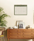 Nail Your 2026 to 2027 Game Plan With This 18 Month Wall Calendar Spanning August 2026 to December 2027 in Green with Twin Wire Binding displayed on a wall.