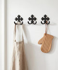 Built Like A Tank 8 Pack Double Wall Hooks Heavy Duty Wrought Iron Cast Iron Vintage Hangers holding an apron and wooden mitt on wall.