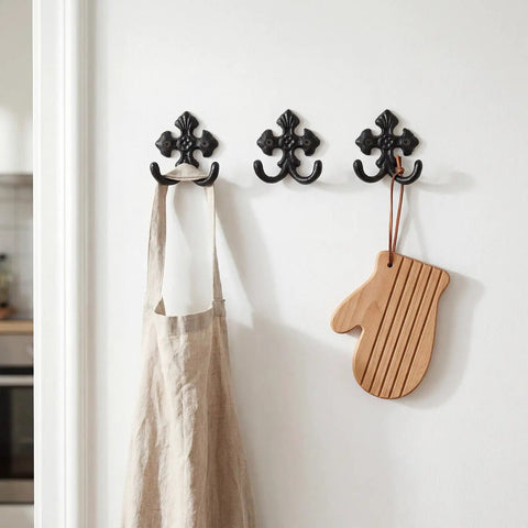 Built Like A Tank 8 Pack Double Wall Hooks Heavy Duty Wrought Iron Cast Iron Vintage Hangers holding an apron and wooden mitt on wall.