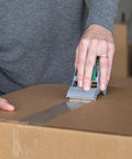 Person using EZ Start Packing Tape With One Handed Dispenser 1.88 Inch By 55.5 Yard Crystal Clear Tape Roll to seal a box.
