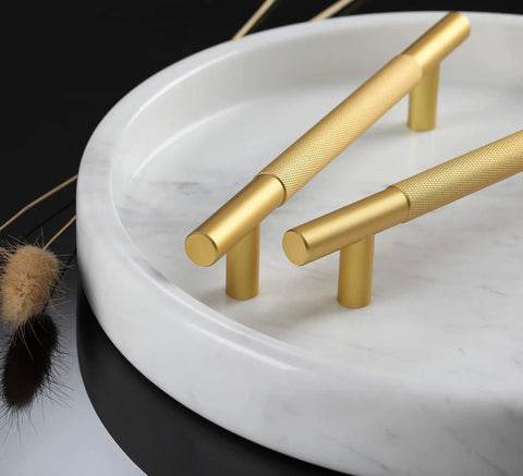 Gold knurled cabinet handles on a white marble plate